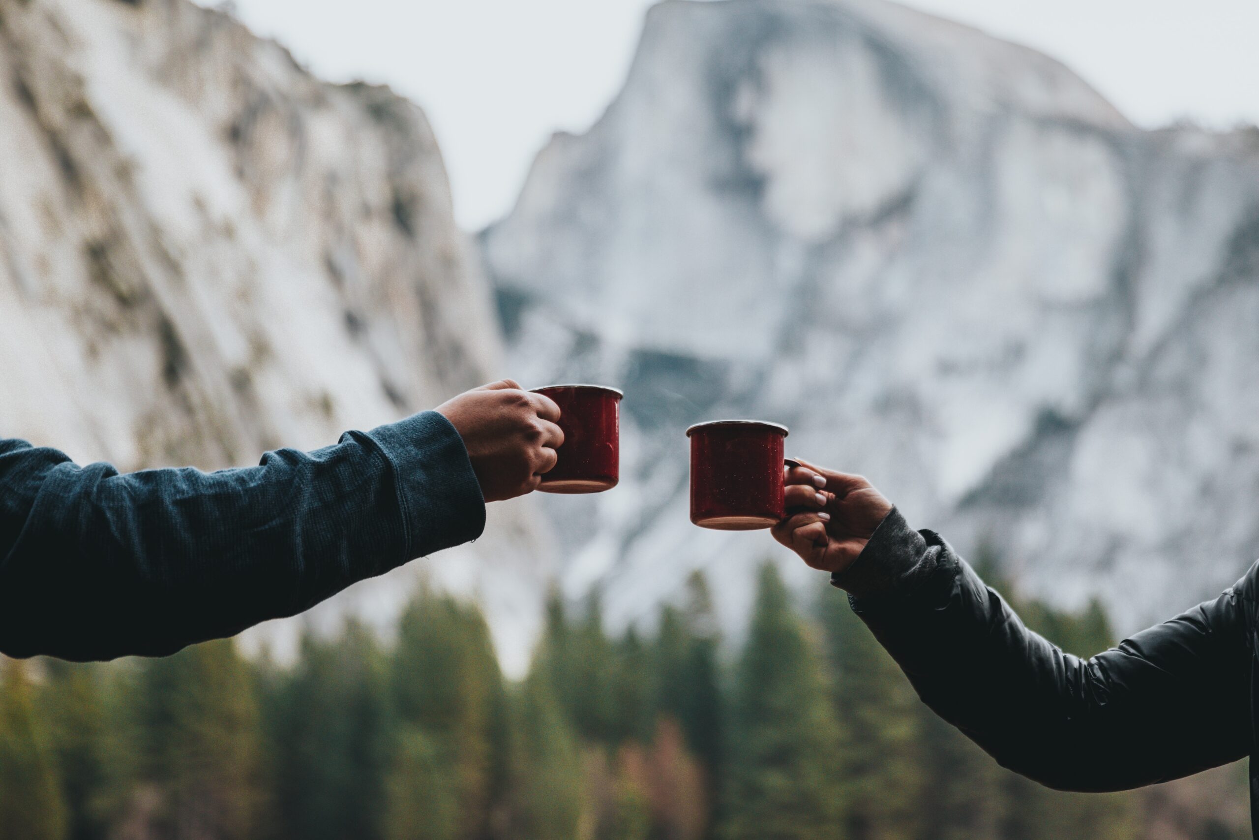 Two outstretched arms holding camping mugs